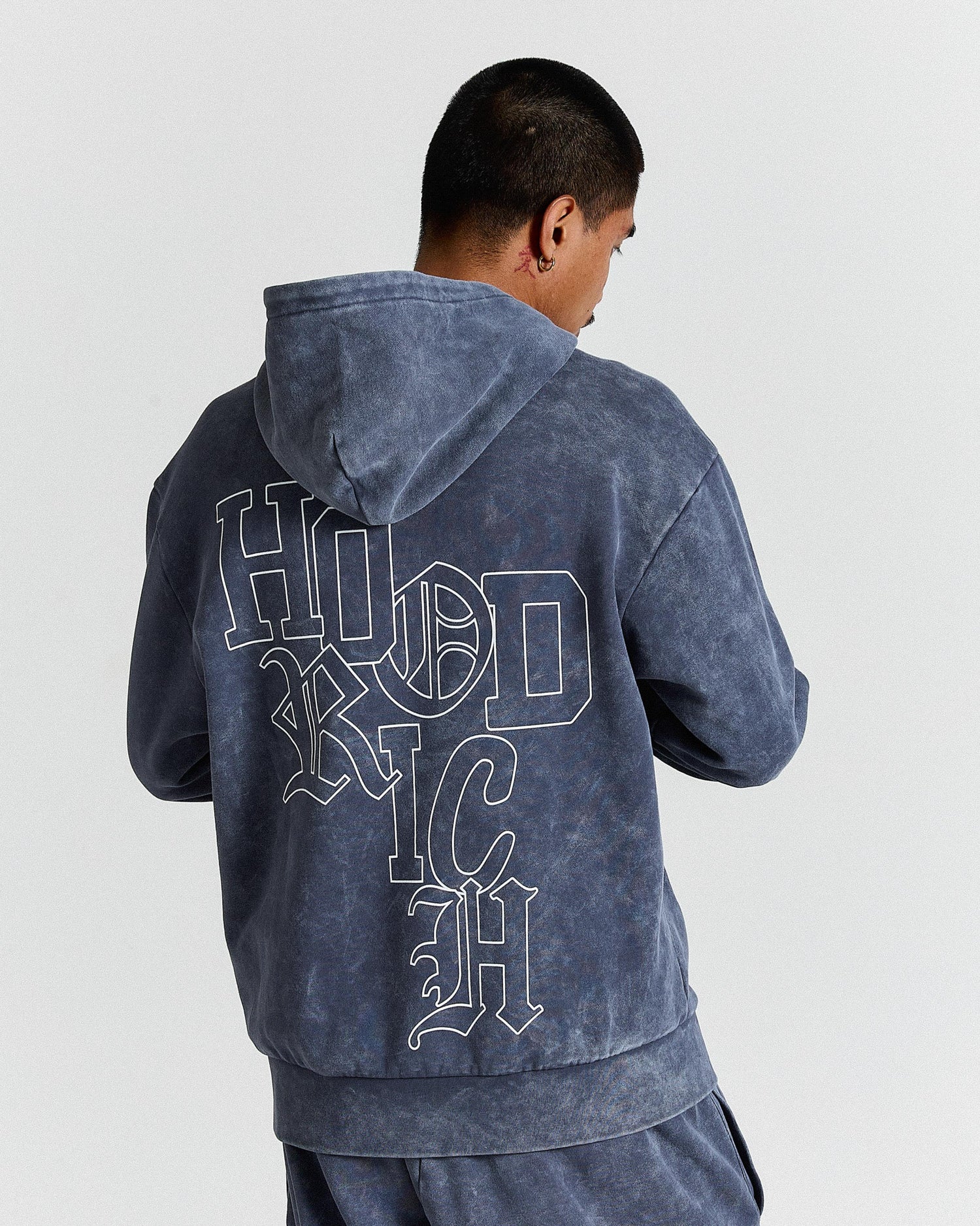 Person wearing a blue hoodie with 'HOODRICH' text on the back against a white background.
