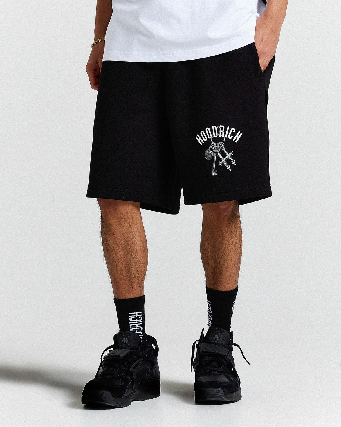 Person wearing black shorts with a logo and text, standing against a white background