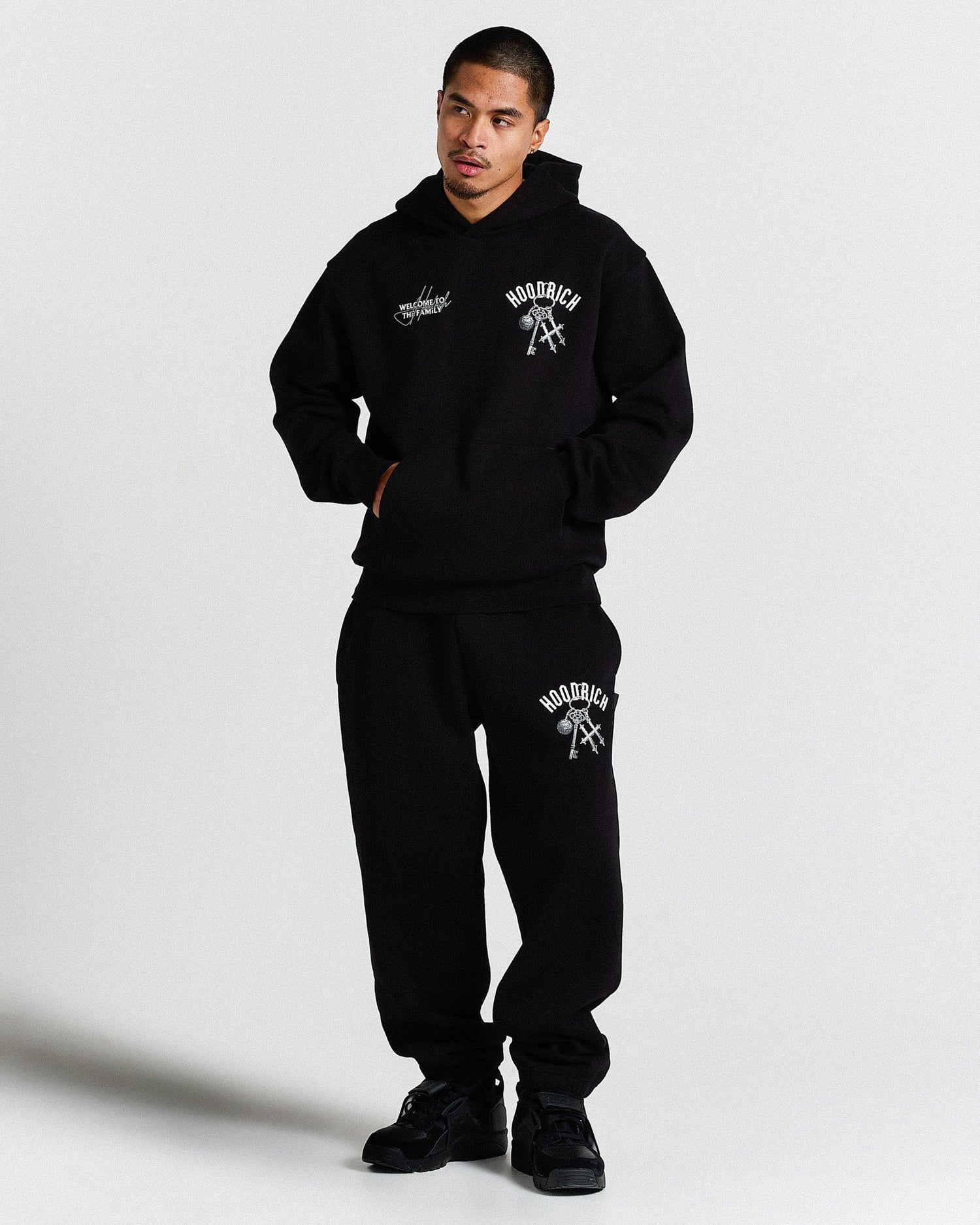 Person wearing a black hoodie and sweatpants set with visible branding on a light gray background