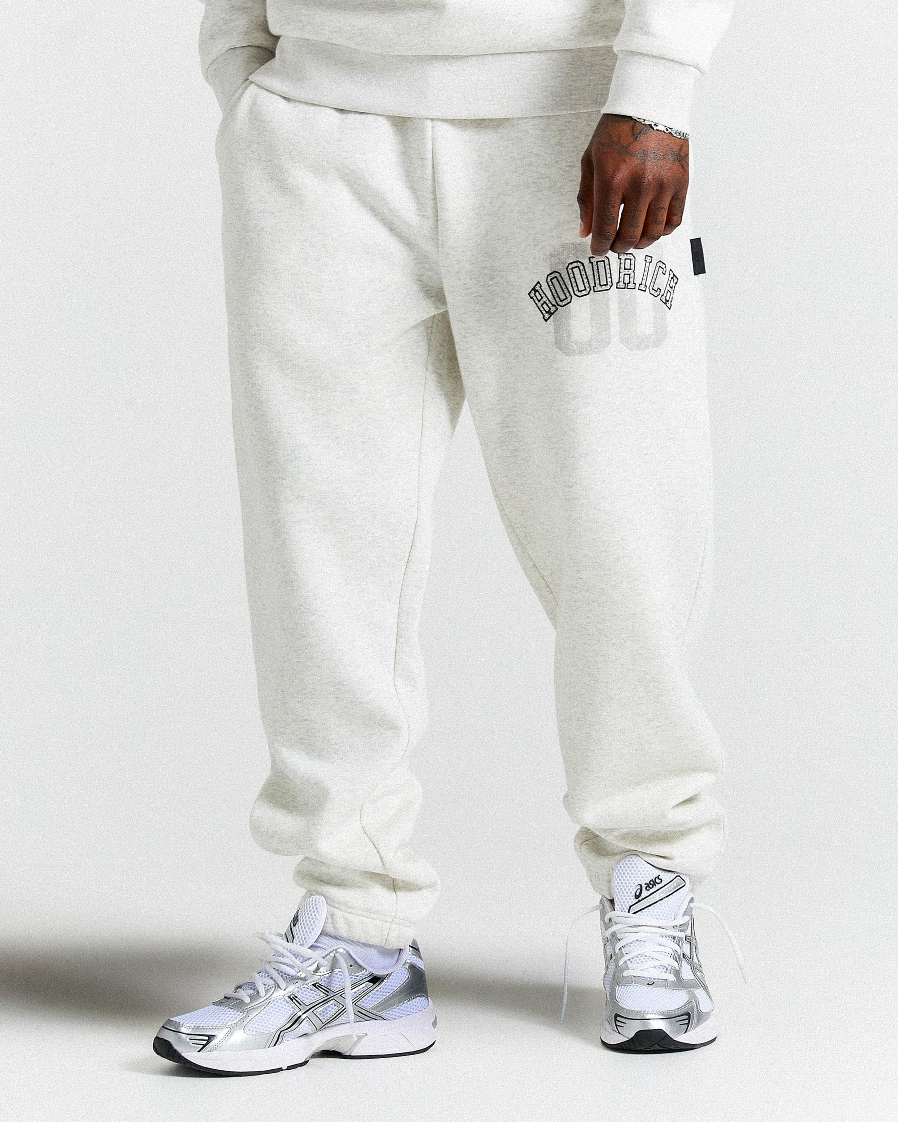 Person wearing light grey sweatpants with a brand logo and white sneakers on a white background