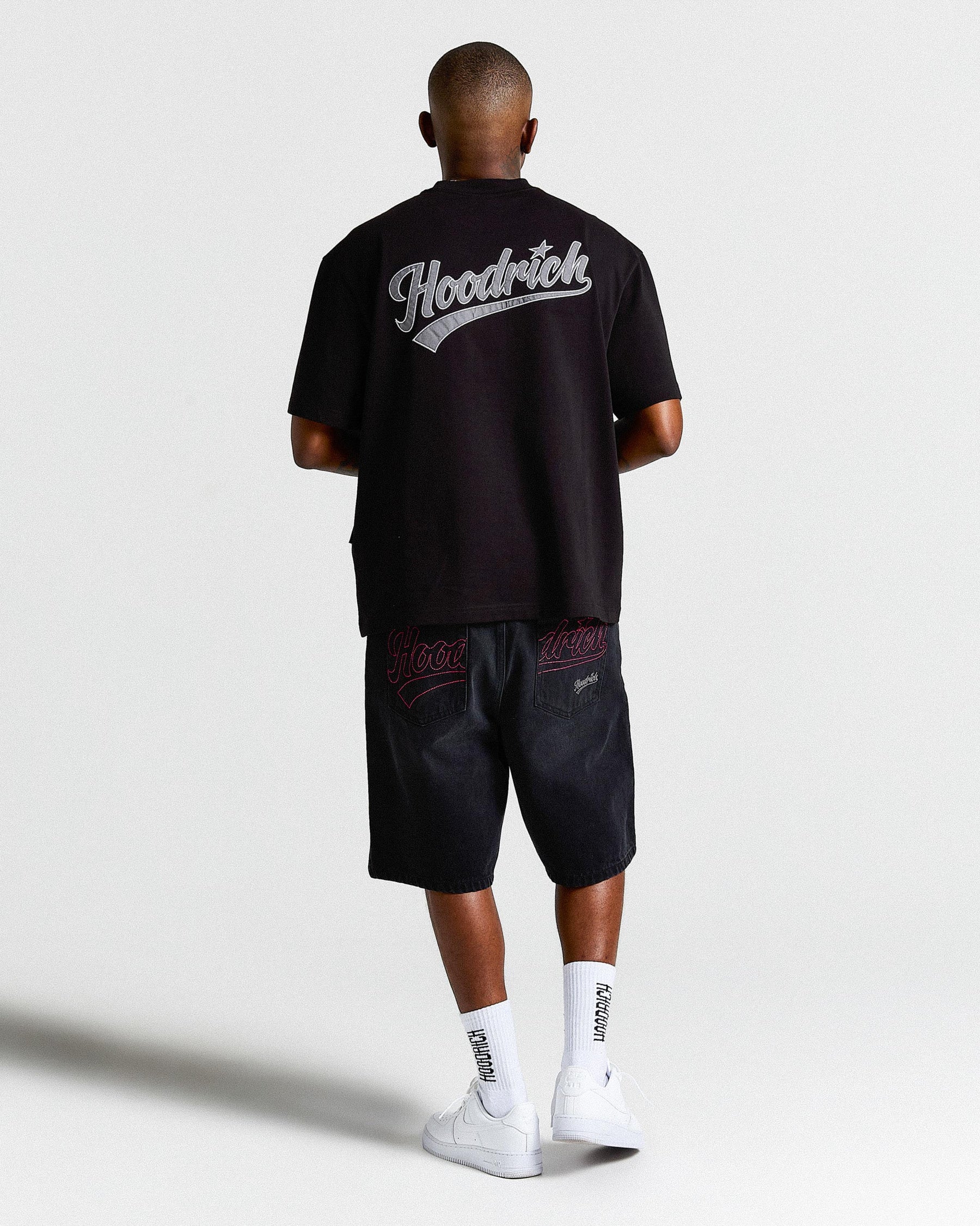 Person wearing a black t-shirt with 'Hoodrich' branding and black shorts on a white background