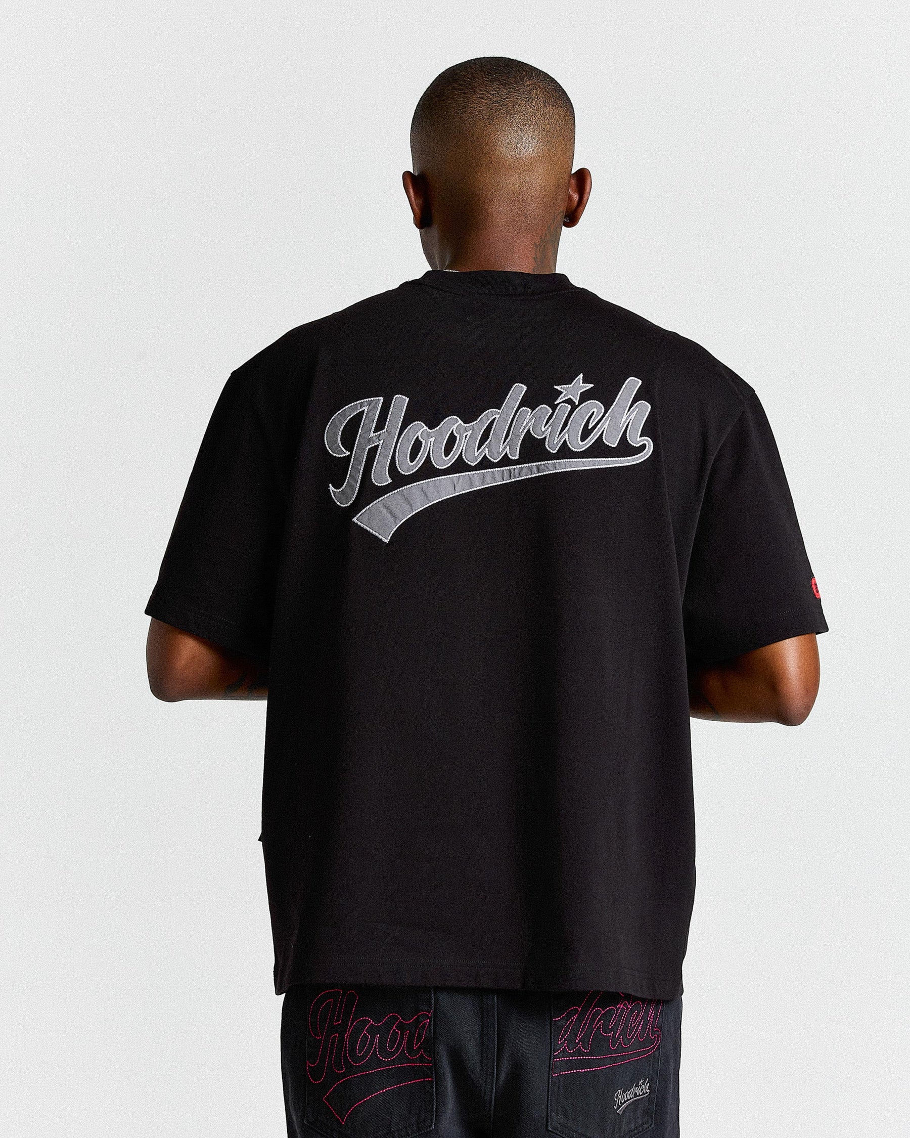 Person wearing a black 'Hoodrich' t-shirt with branding on the back against a white background