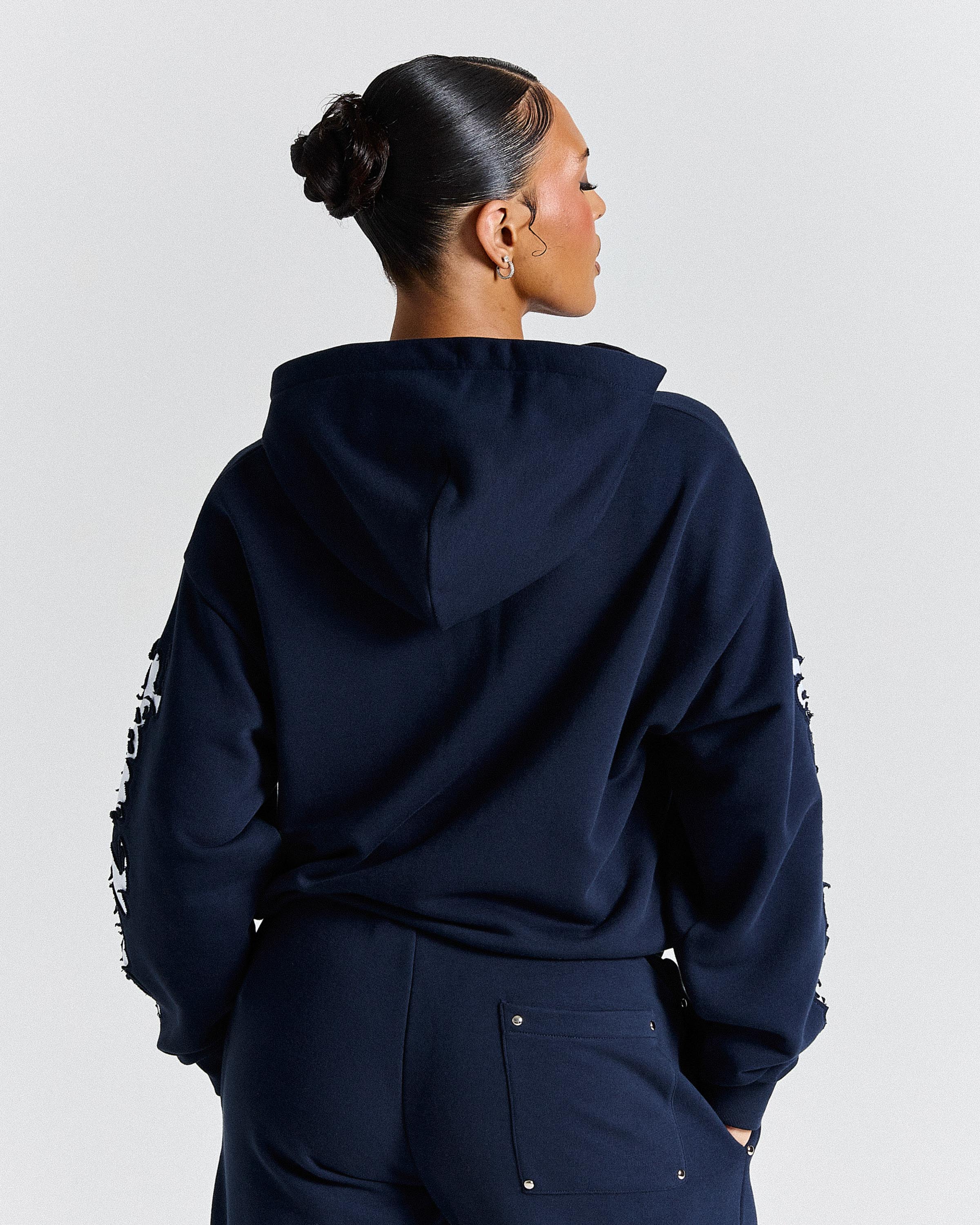 Person wearing a navy blue hoodie with white text on sleeves against a light gray background