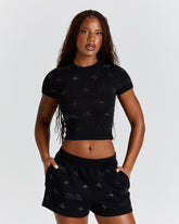 Woman wearing a black crop top and shorts with a pattern on a plain background