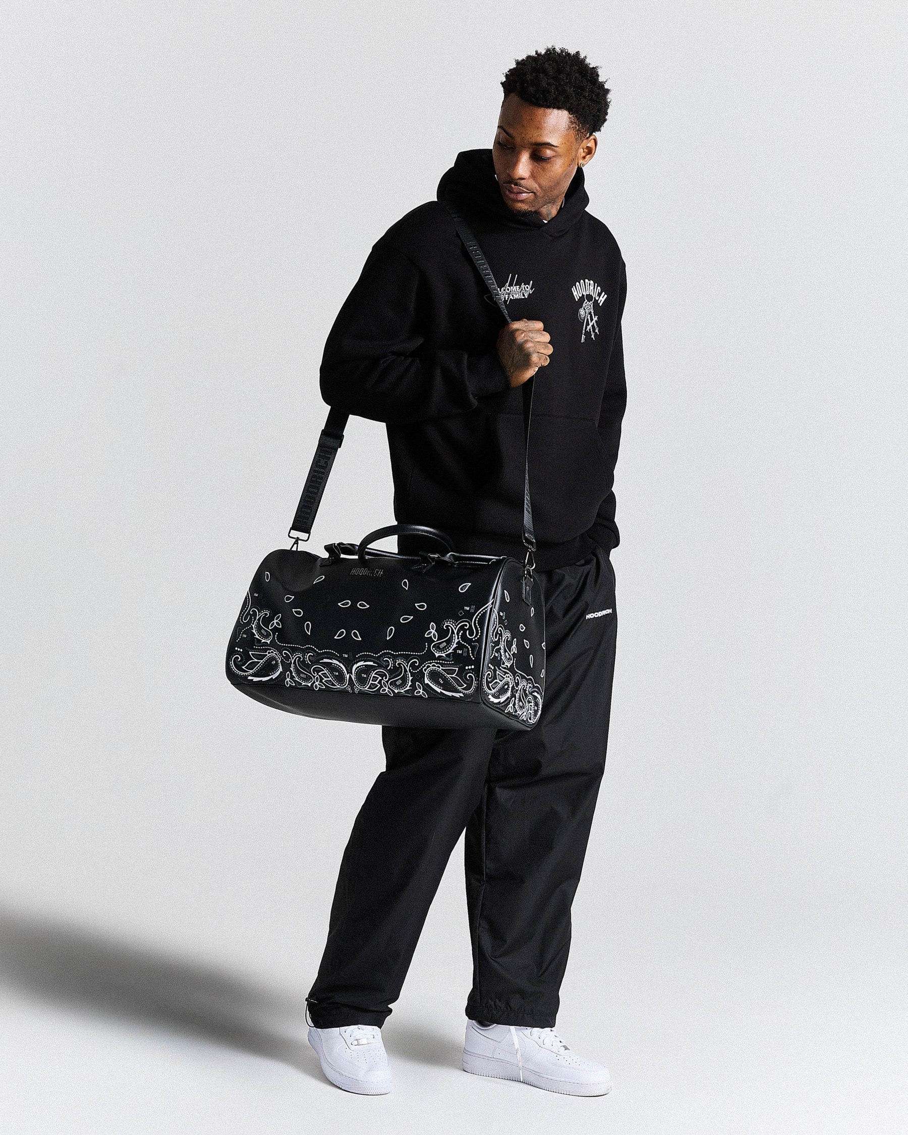 Man holding a black duffel bag with a pattern against a light gray background