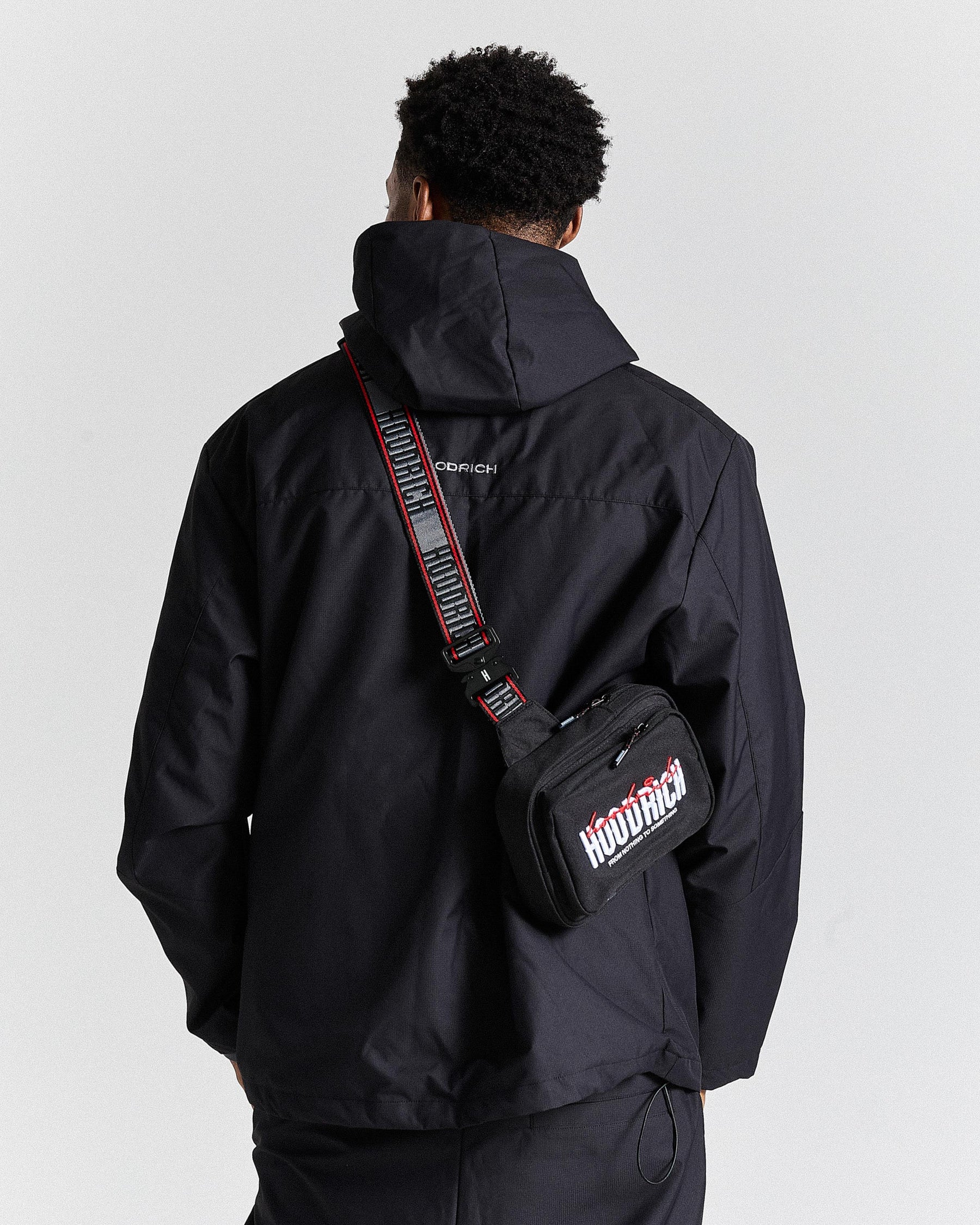 Person wearing a black jacket with a black bag featuring white and red text on a white background