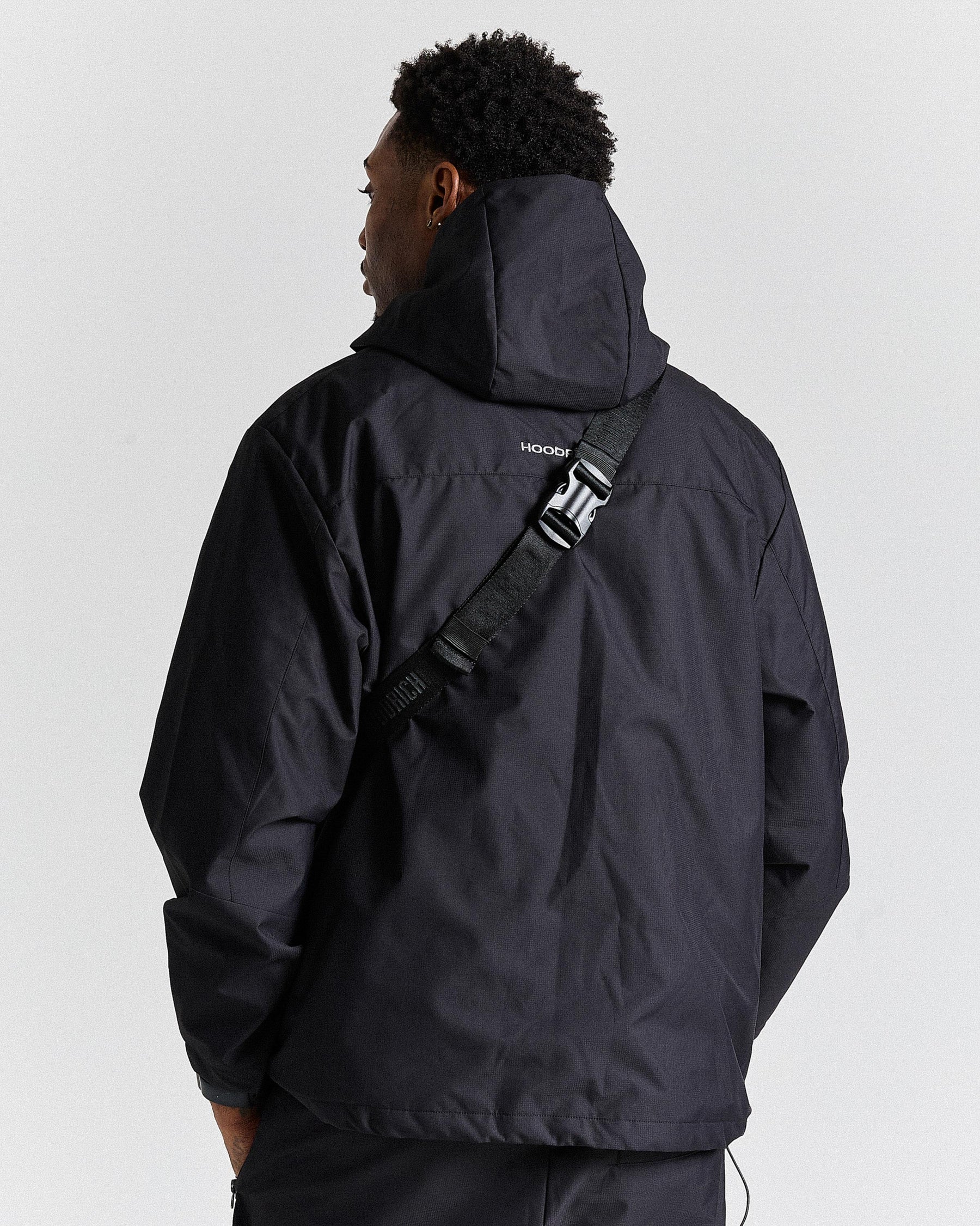 Person wearing a black jacket with a visible brand logo on a light gray background