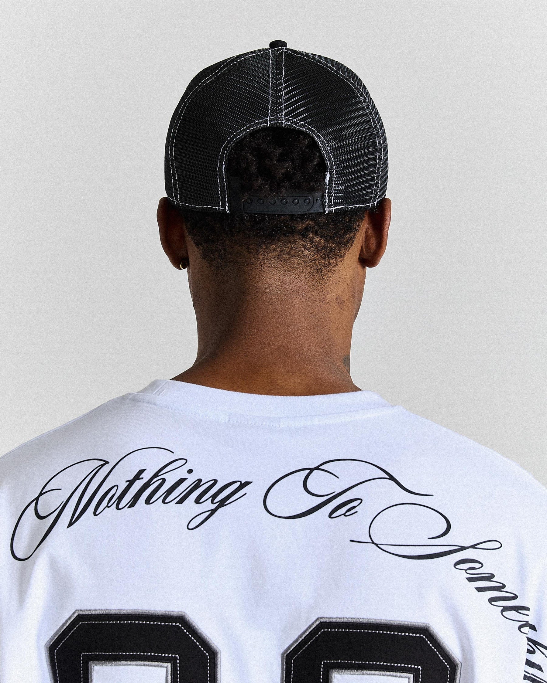 Person wearing a black cap and white shirt with text on the back against a plain background