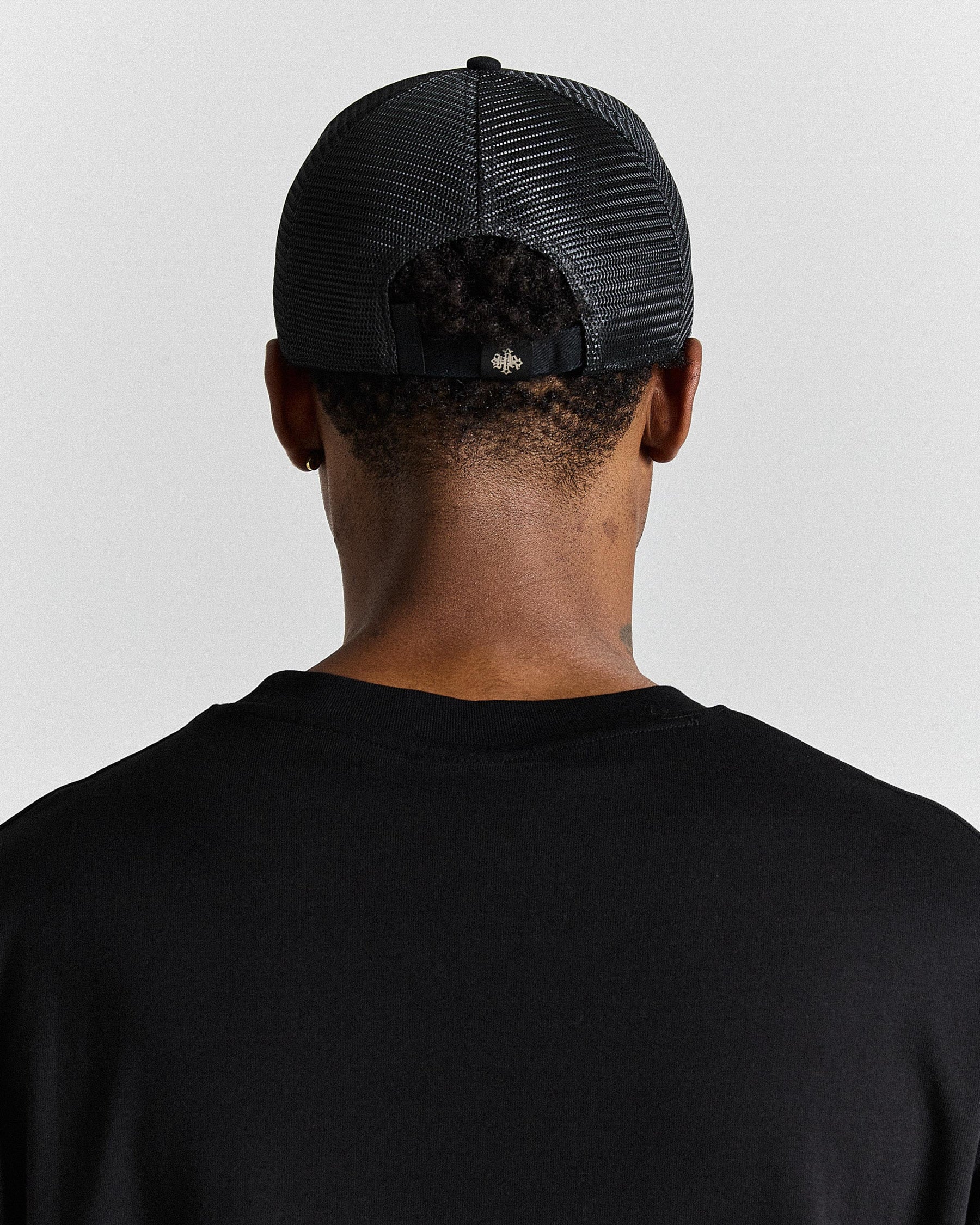 Person wearing a black mesh cap and black shirt on a light gray background