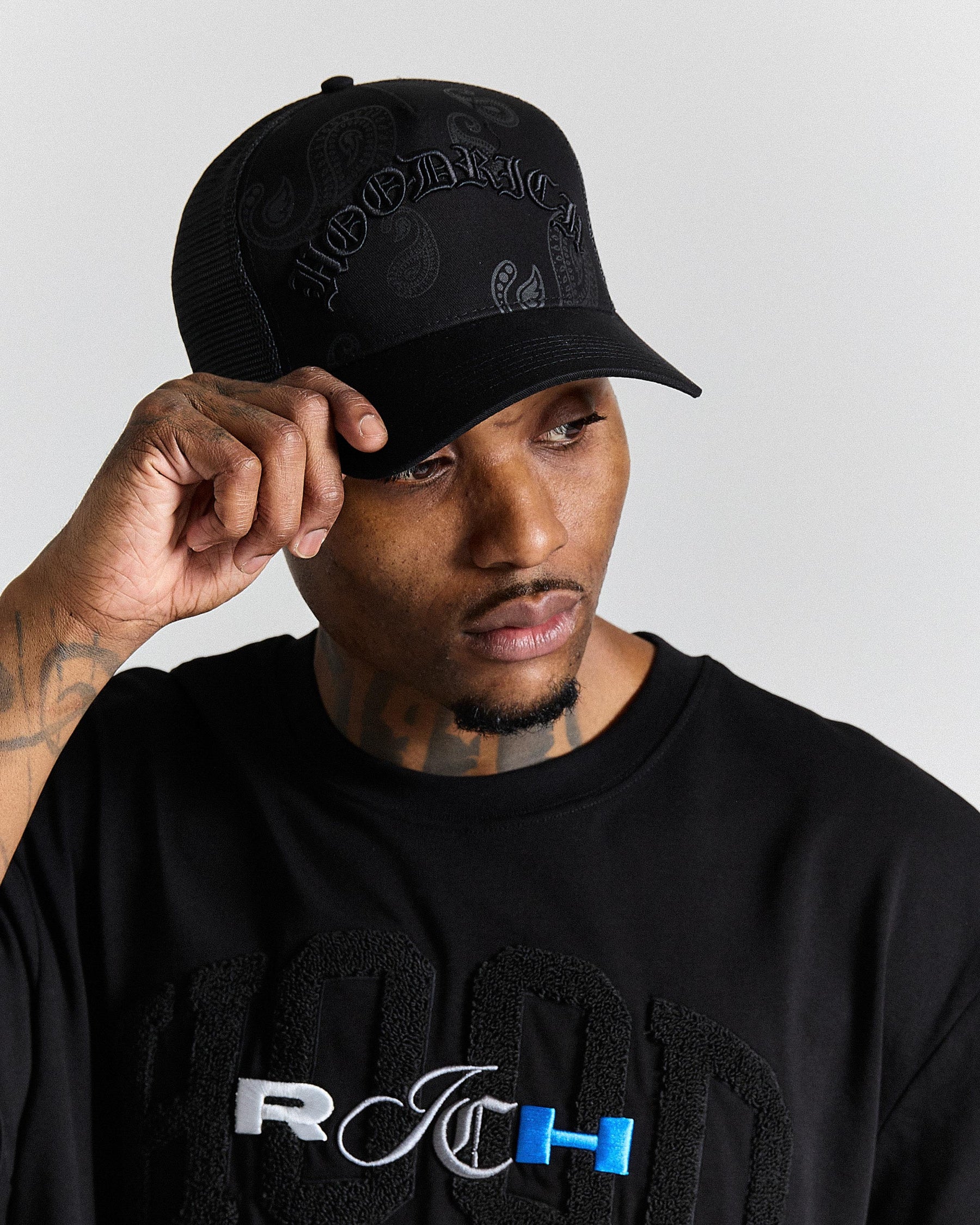 Man wearing a black cap and black shirt with logo, against a plain background