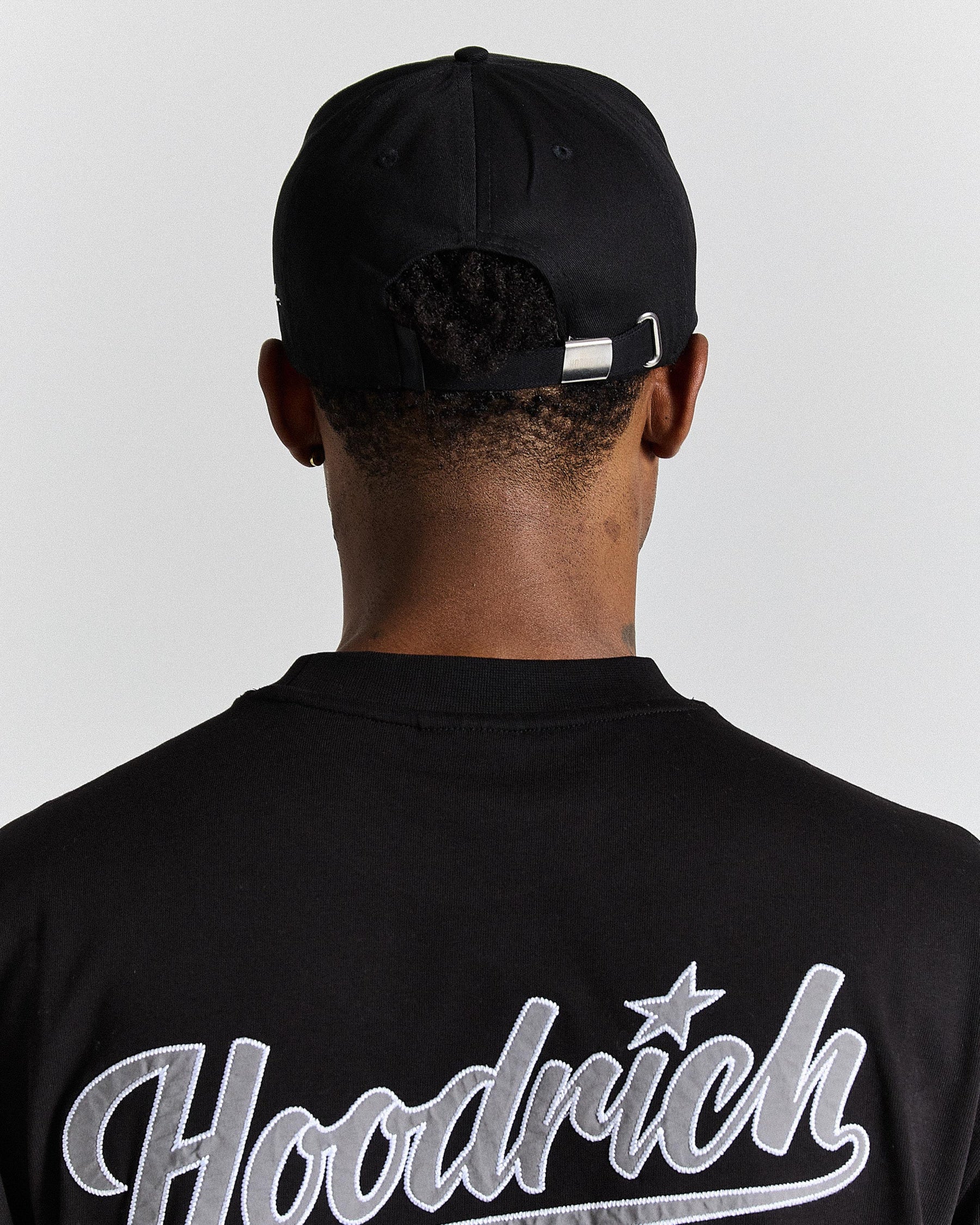 Person wearing a black cap and black shirt with 'Hoodrich' branding on a light gray background