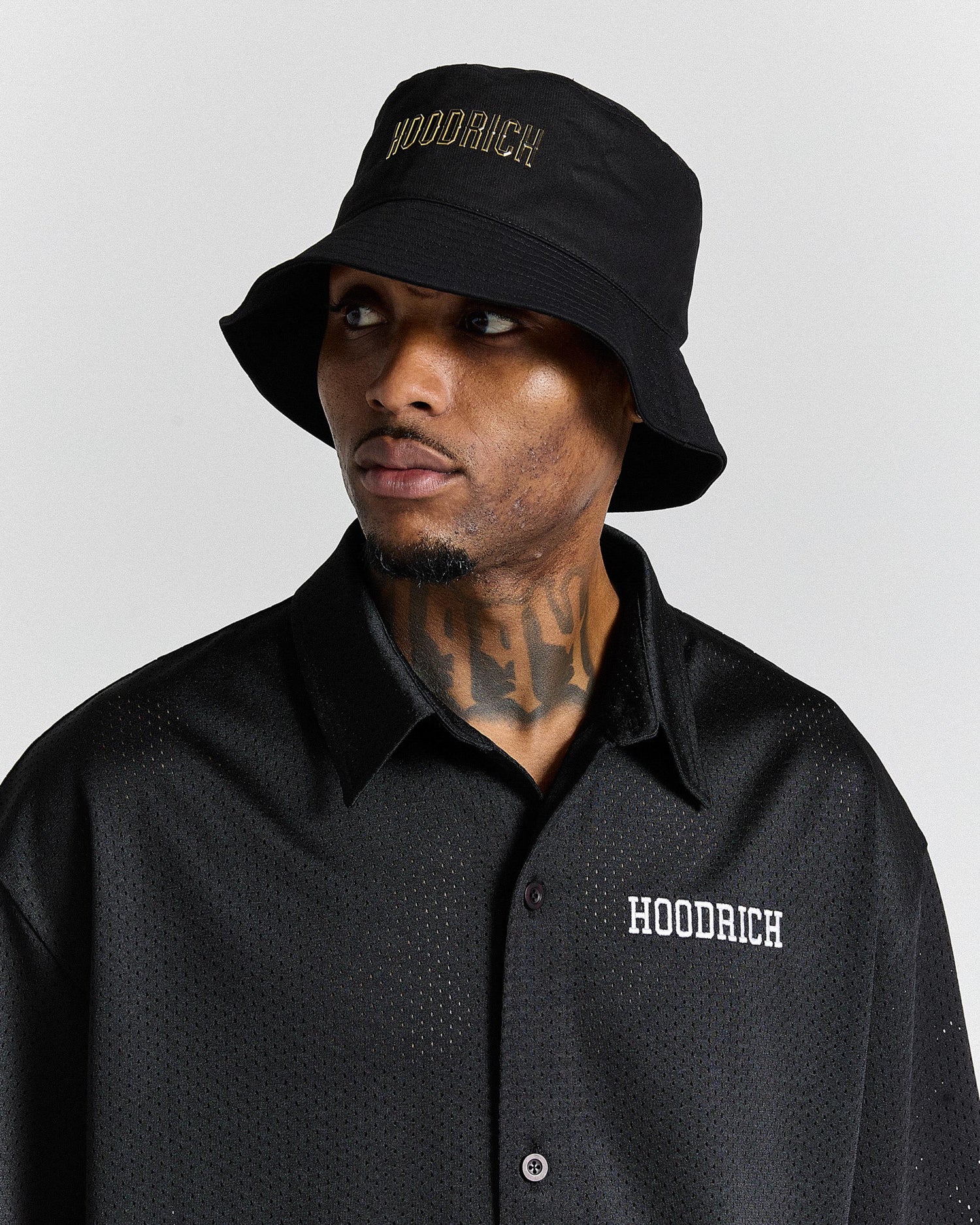 Man wearing a black 'Hoodrich' bucket hat and shirt against a gray background