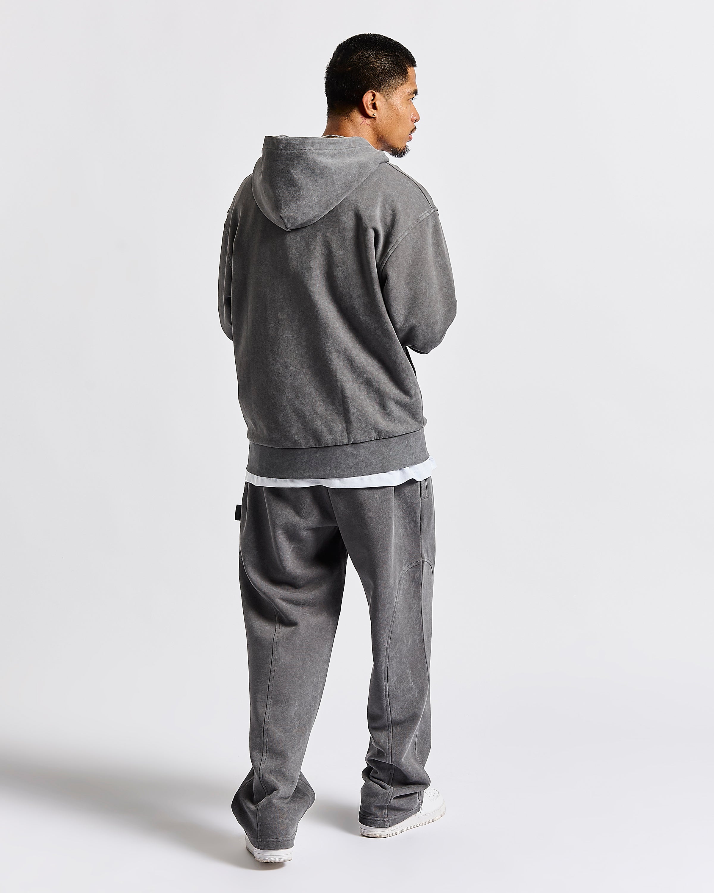 A man wearing a gray hooded sweatshirt and matching gray sweatpants, shown from the back against a light gray studio background.