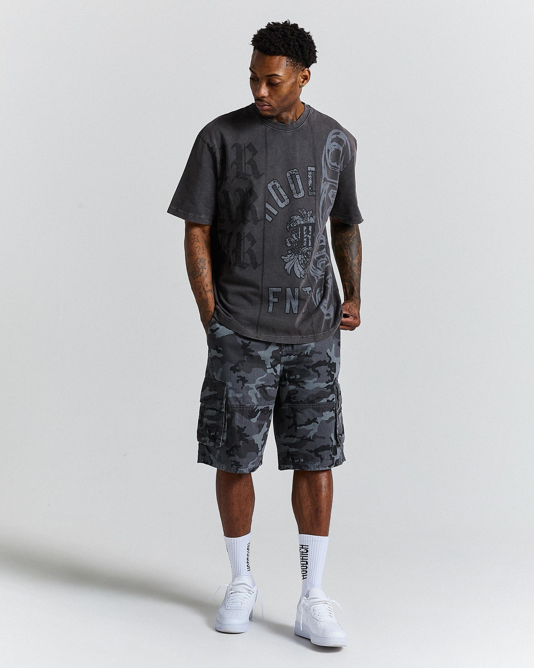 Man wearing a black graphic t-shirt and camouflage shorts on a light grey background