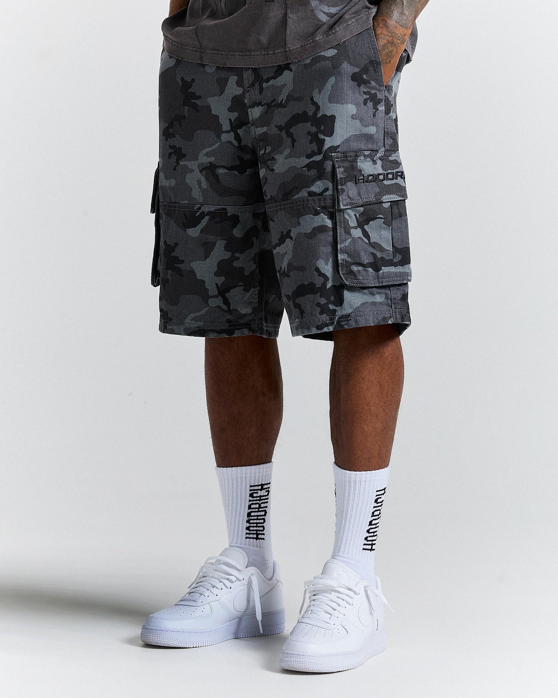 Person wearing camouflage cargo shorts and white sneakers and white socks with black text on a light grey background