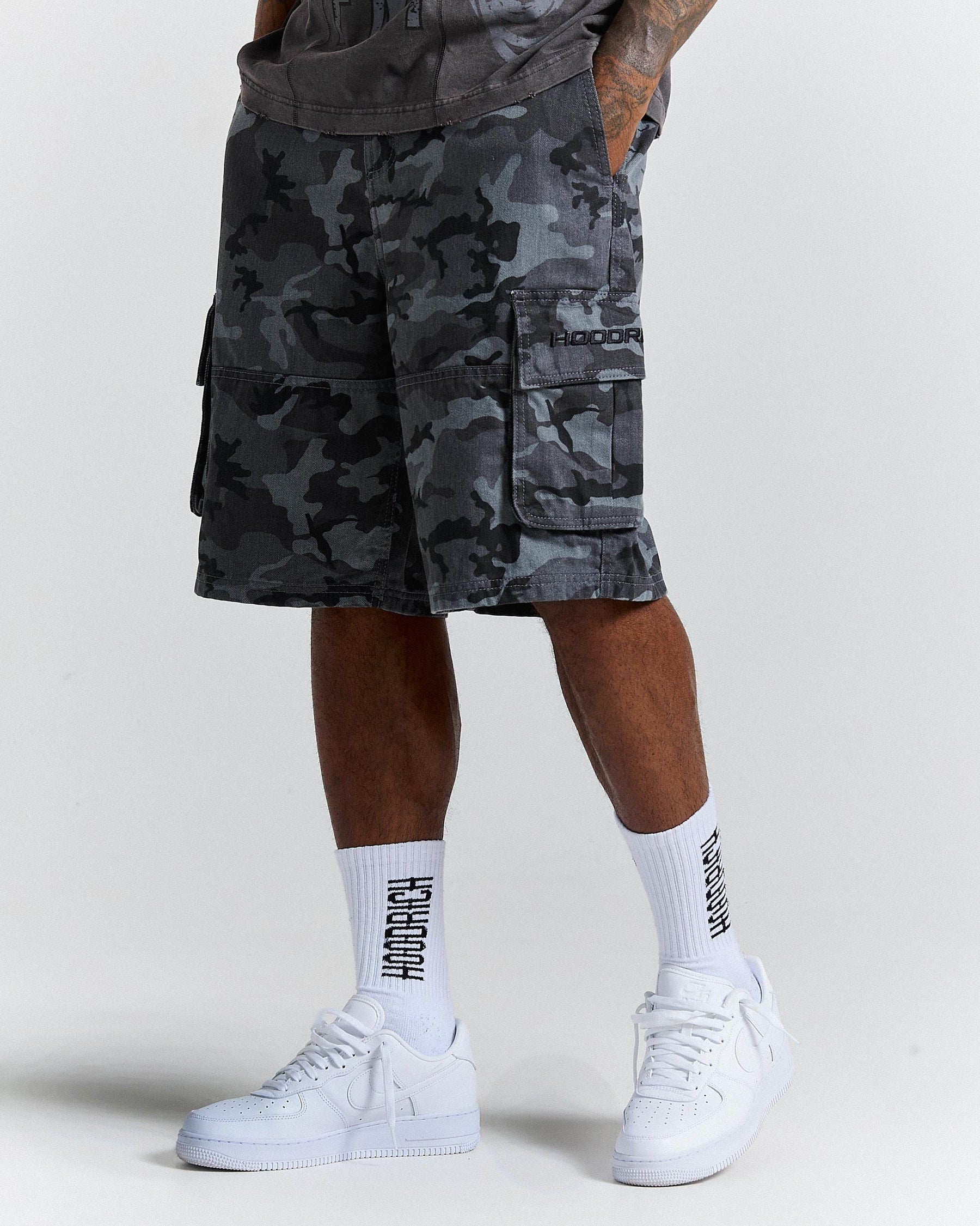 Person wearing camouflage shorts and white sneakers with visible branding on a plain background