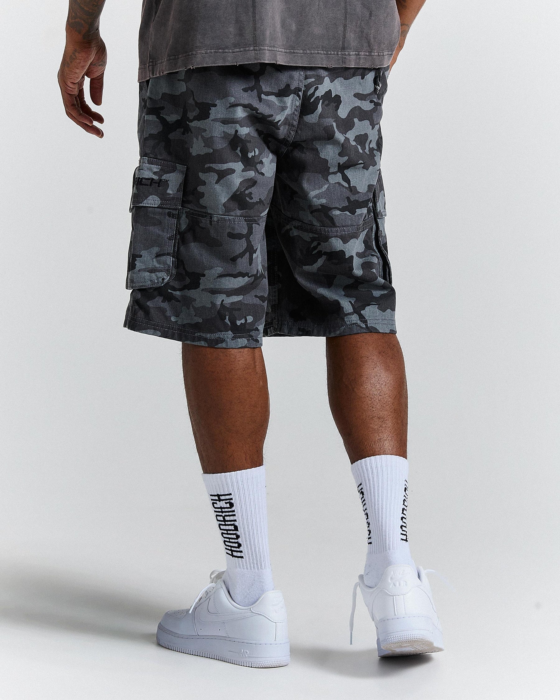 Person wearing camouflage shorts and white sneakers on a plain background