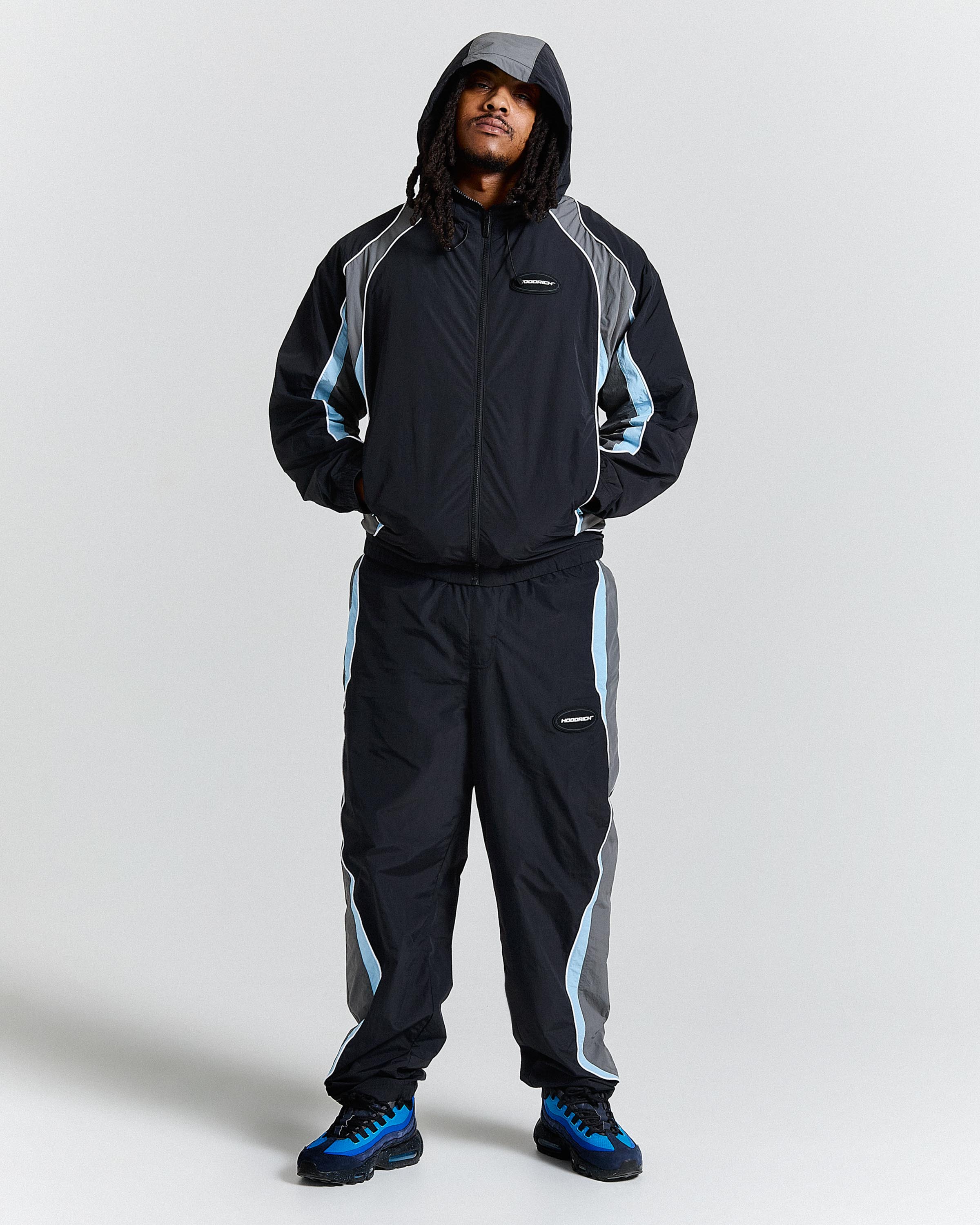 Person wearing a black and gray tracksuit with blue accents on a white background