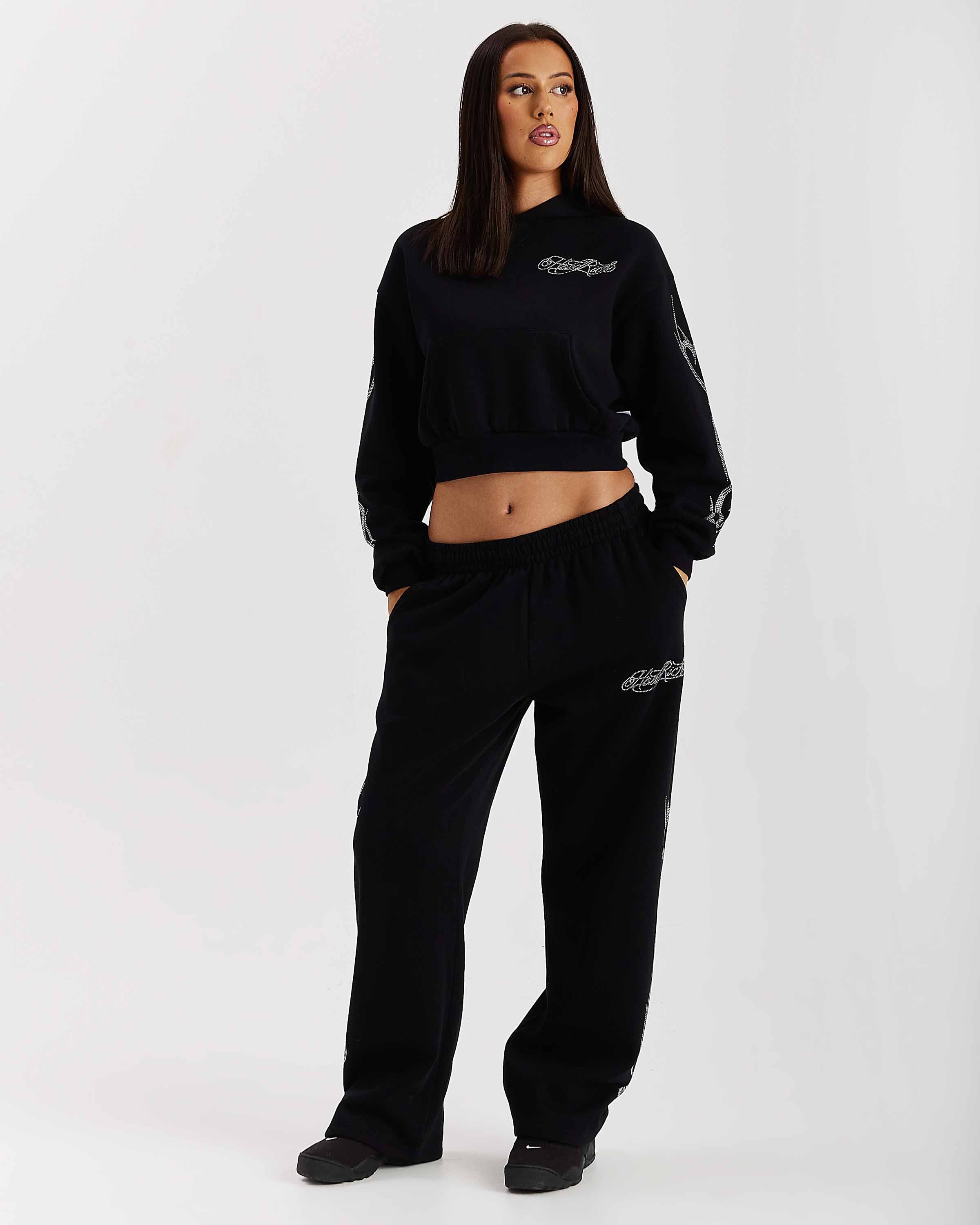 Person wearing a black tracksuit with brand logos on a white background