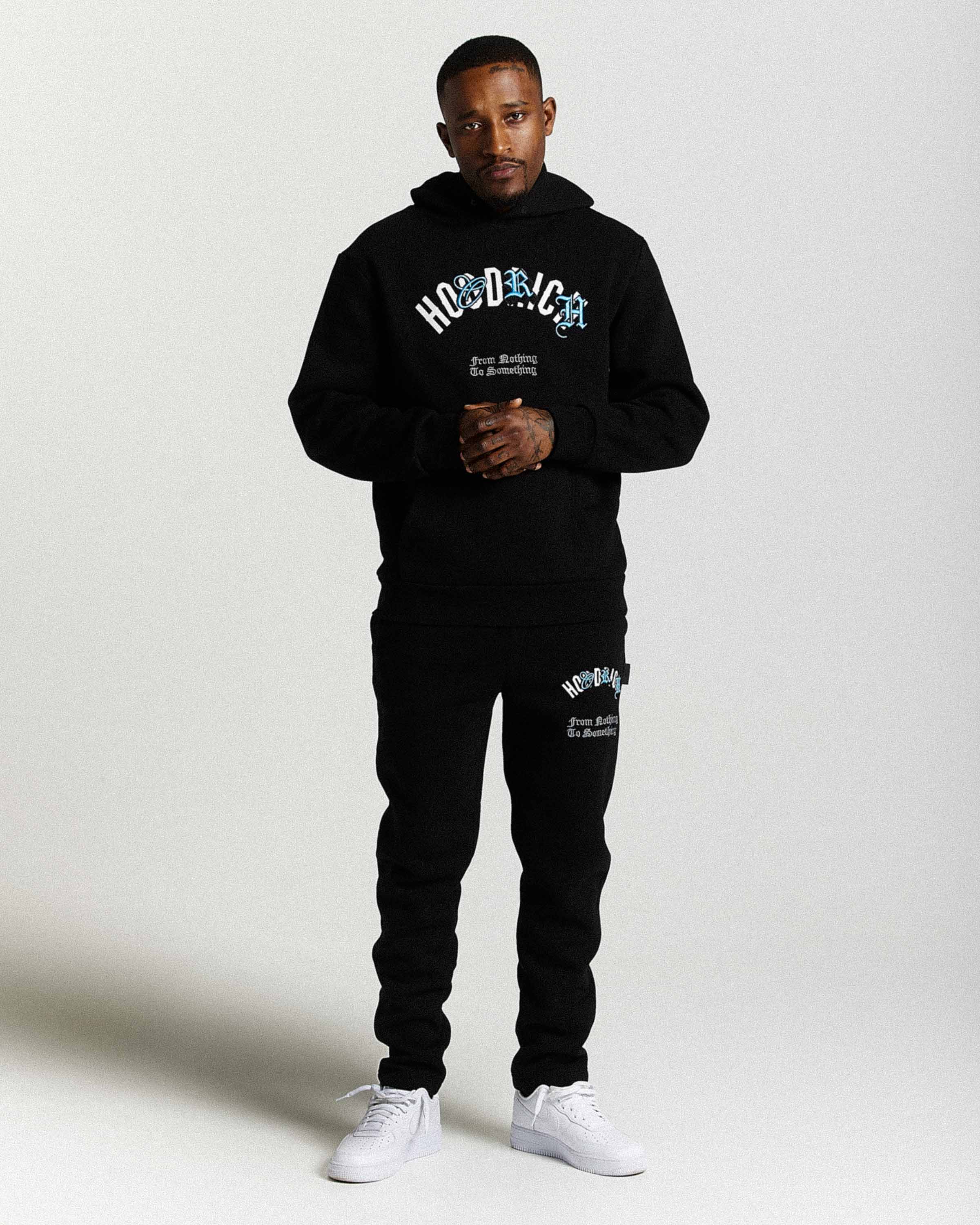 Displays a model wearing the Black 'Hoodrich' branded men's Shadow Full Tracksuit